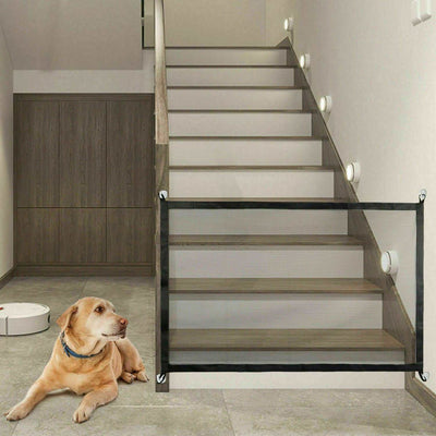 Portable Magic Mesh Pet Safety Gate installed at the base of stairs, featuring a dog in front.